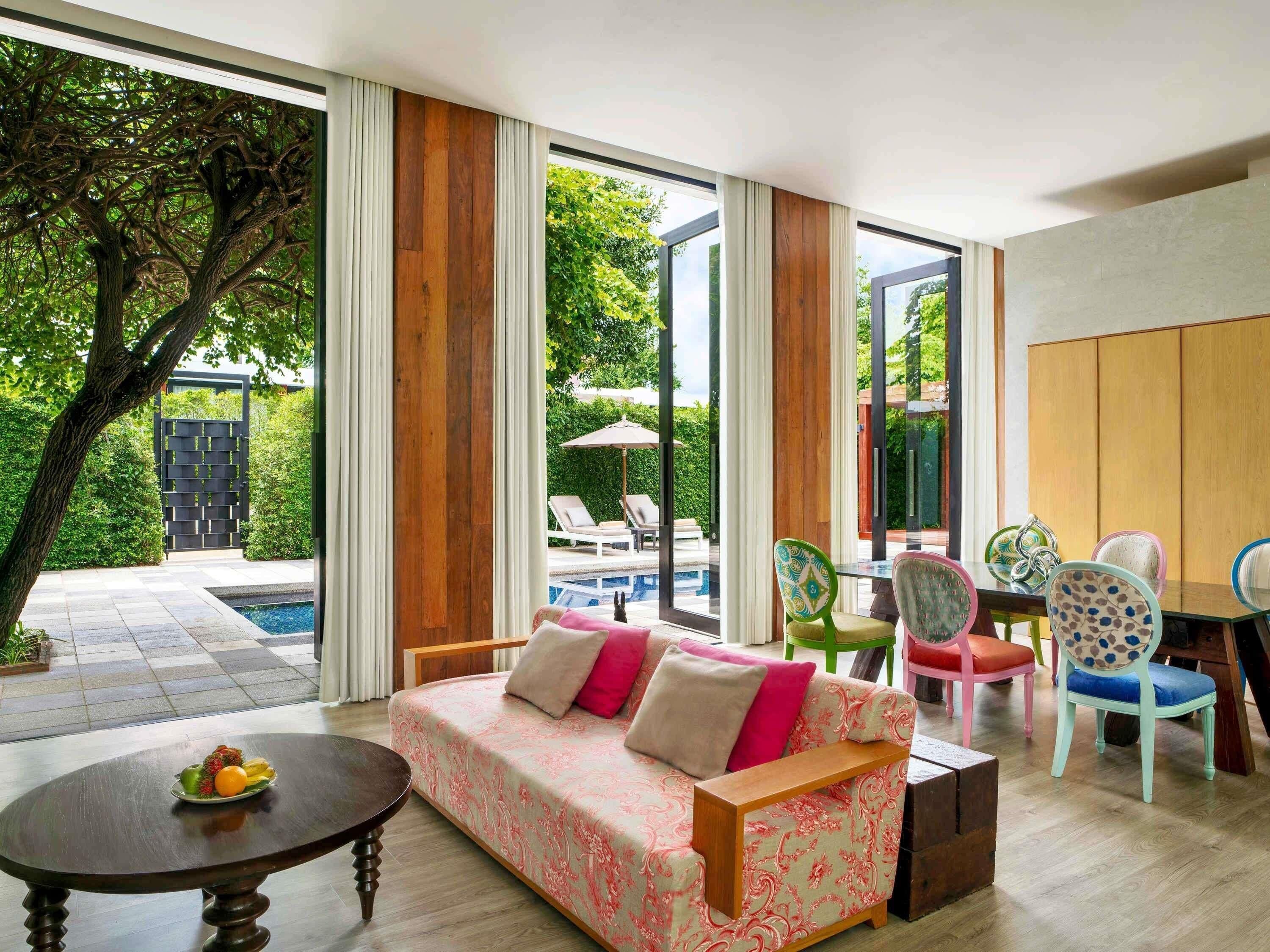 A modern living room with a sofa, chairs, a table, and a view of a pool and garden.