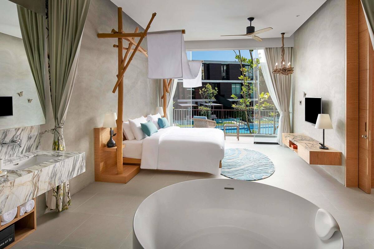 Een moderne hotelkamer met een groot bed, een badkuip, een balkon met zwembad en een televisie.