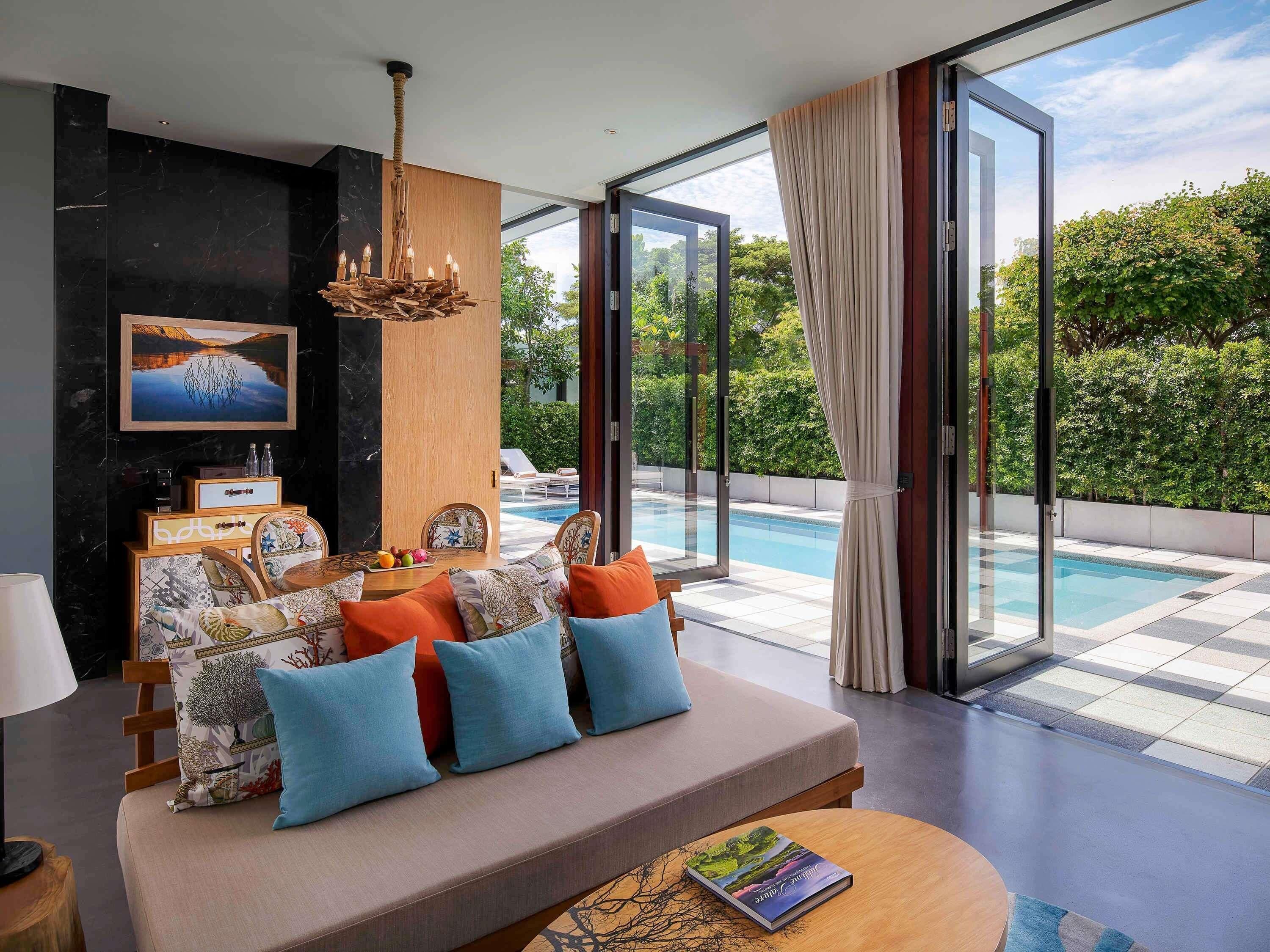 A modern living room with a sofa, a table, and a view of a swimming pool.