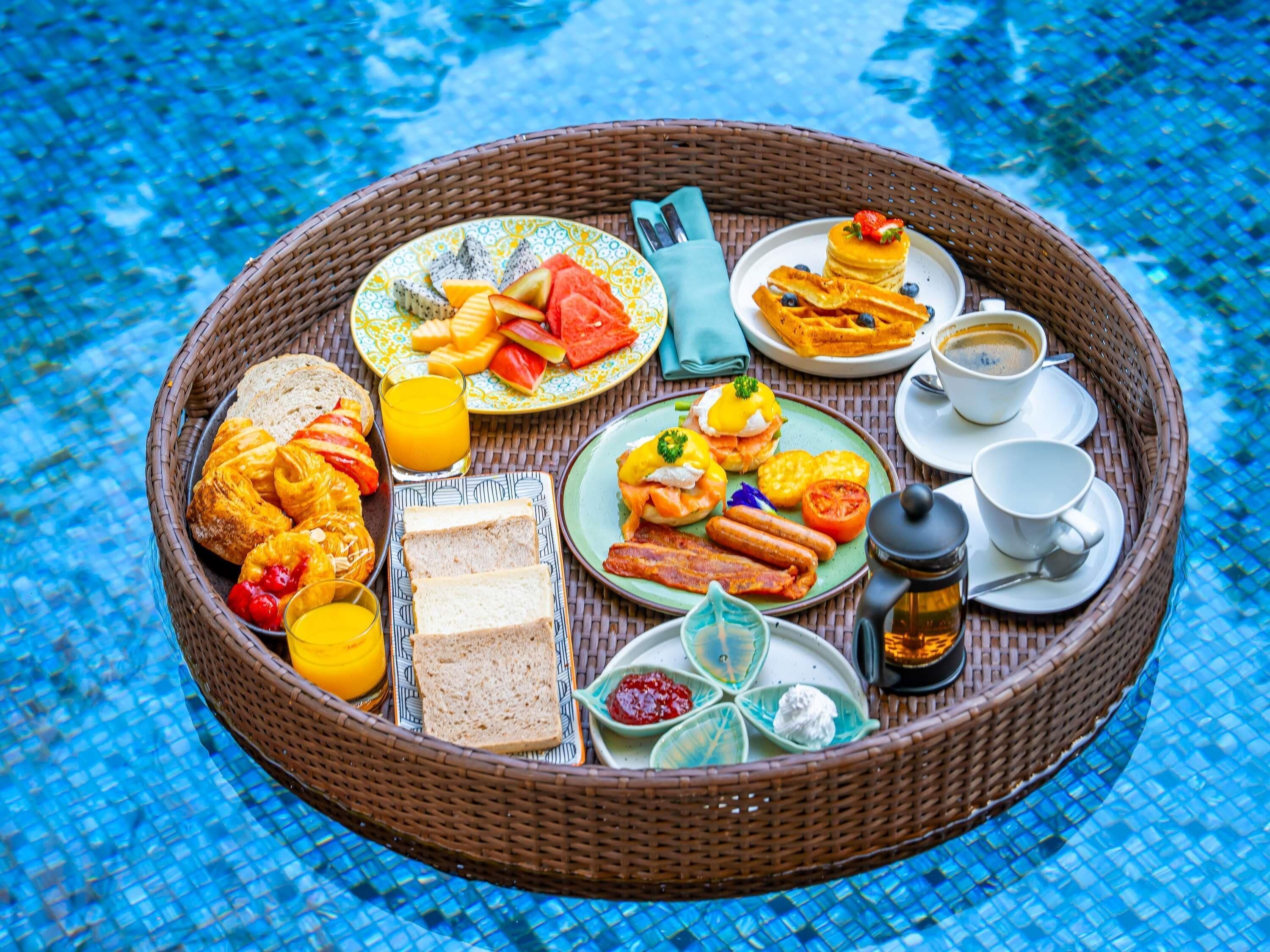 A breakfast tray with various foods and drinks on a poolside table.