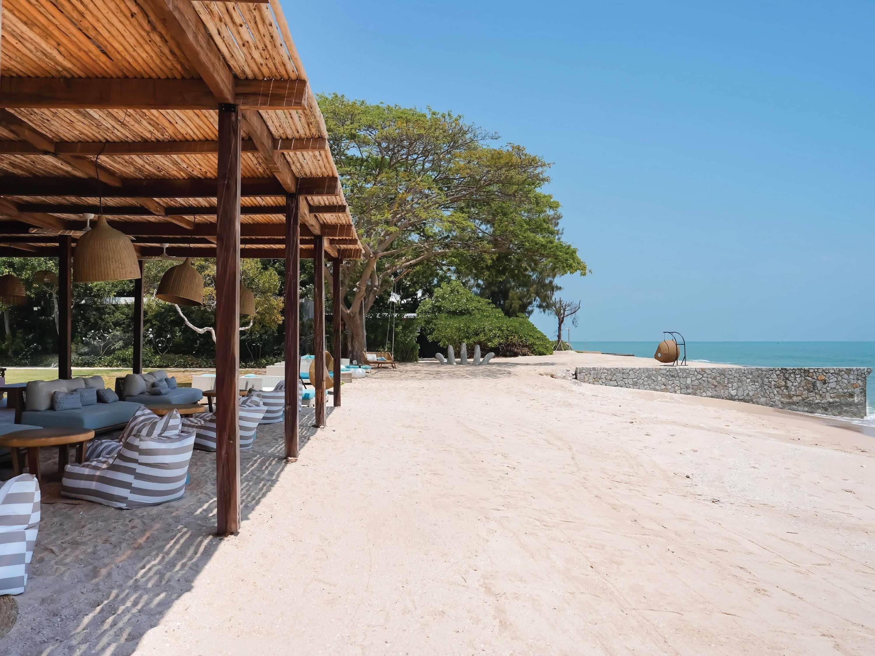 Ein überdachter Außenbereich mit Sofas und Sesseln, einer Steinwand und Blick aufs Meer.