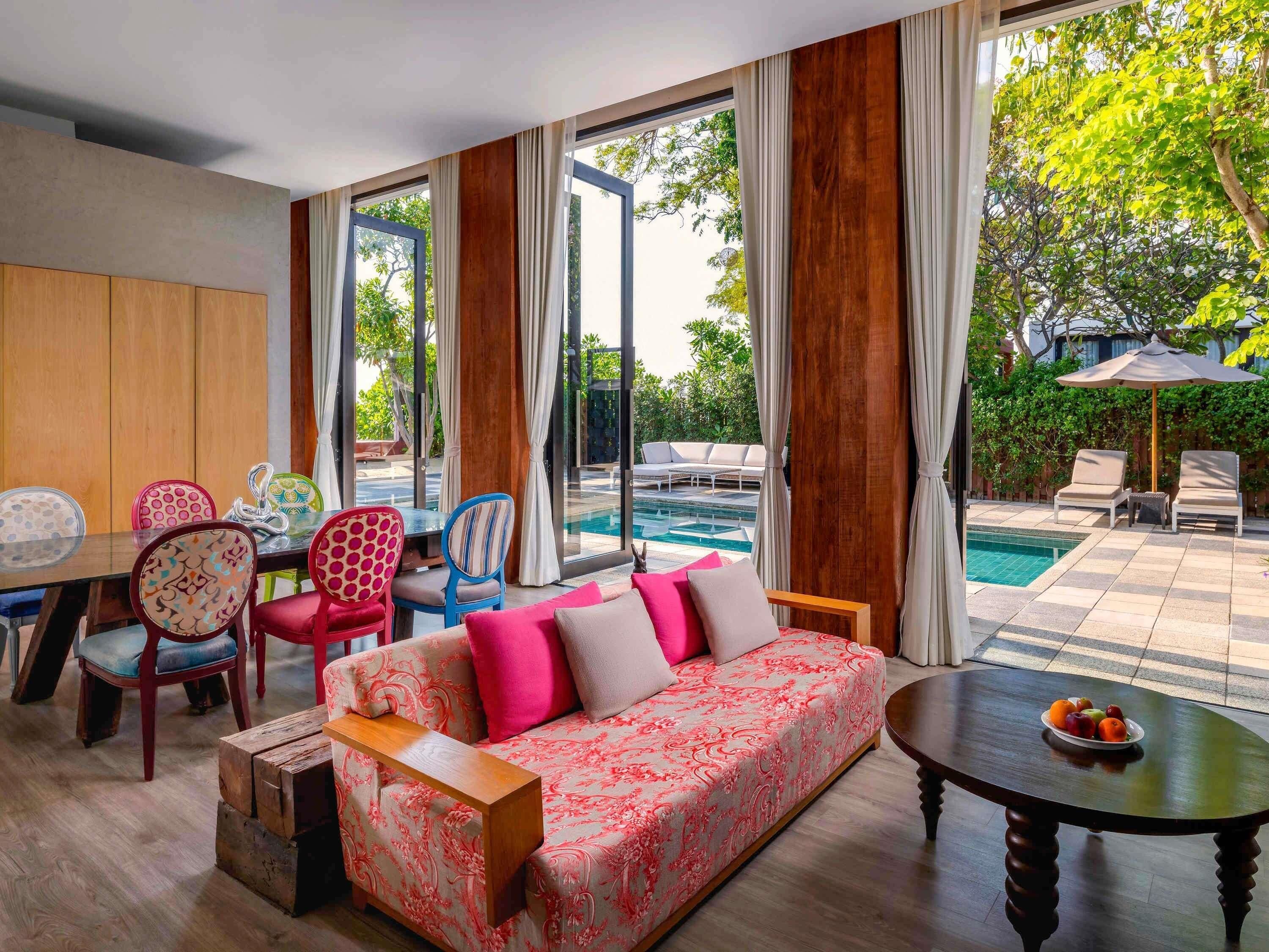 A modern living room with a sofa, chairs, a dining table, and a view of a swimming pool.