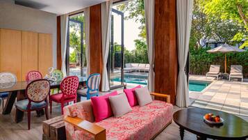 A modern living room with a sofa, chairs, a dining table, and a view of a swimming pool.