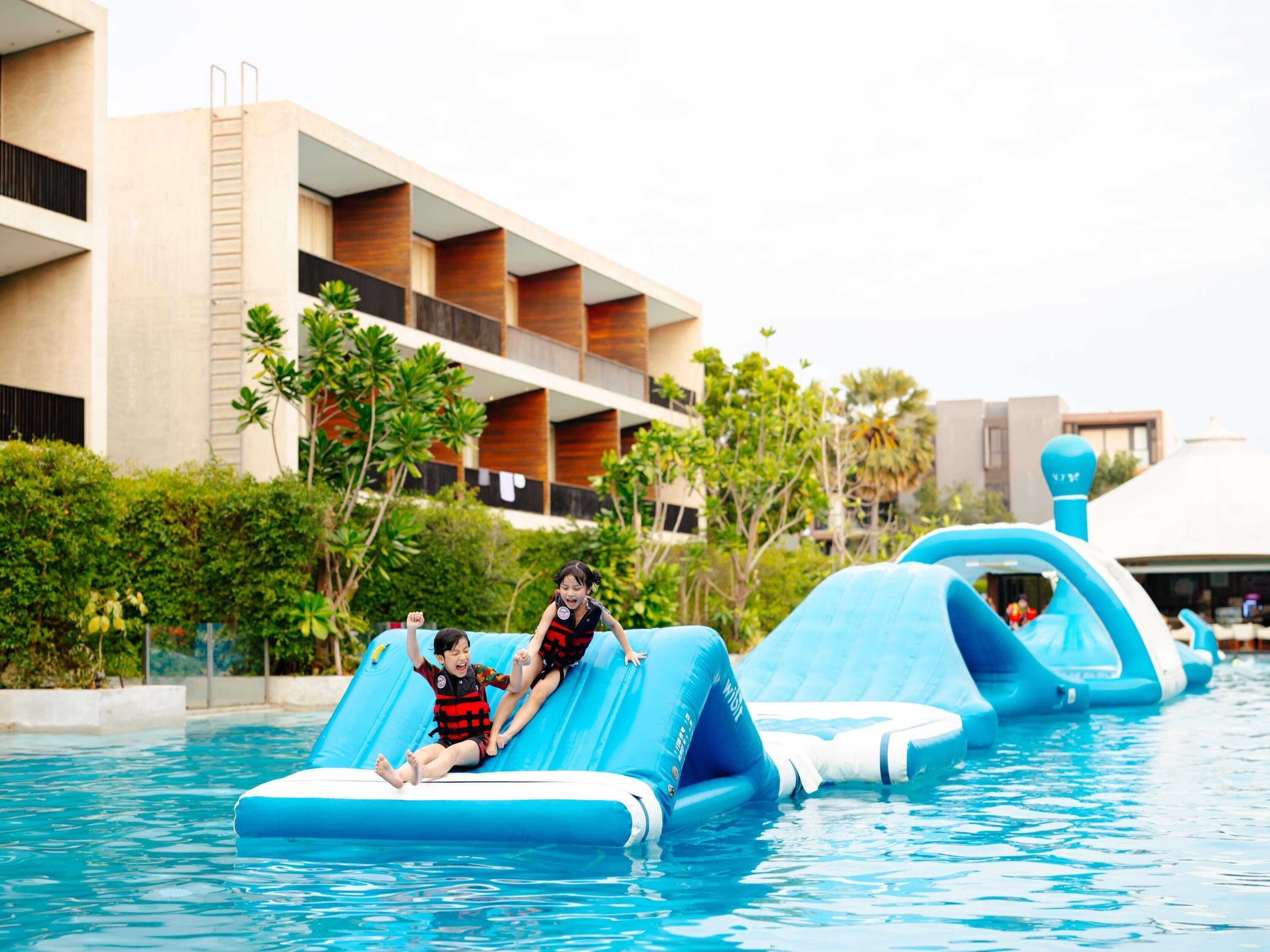 A swimming pool with inflatable slides and a hotel building in the background.
