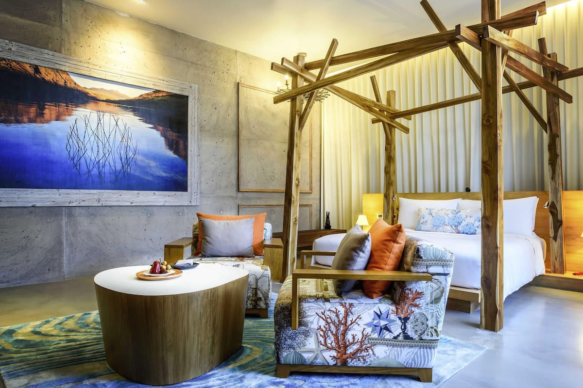 A room with a bed, a wooden chair, a round table, and a painting of a landscape.
