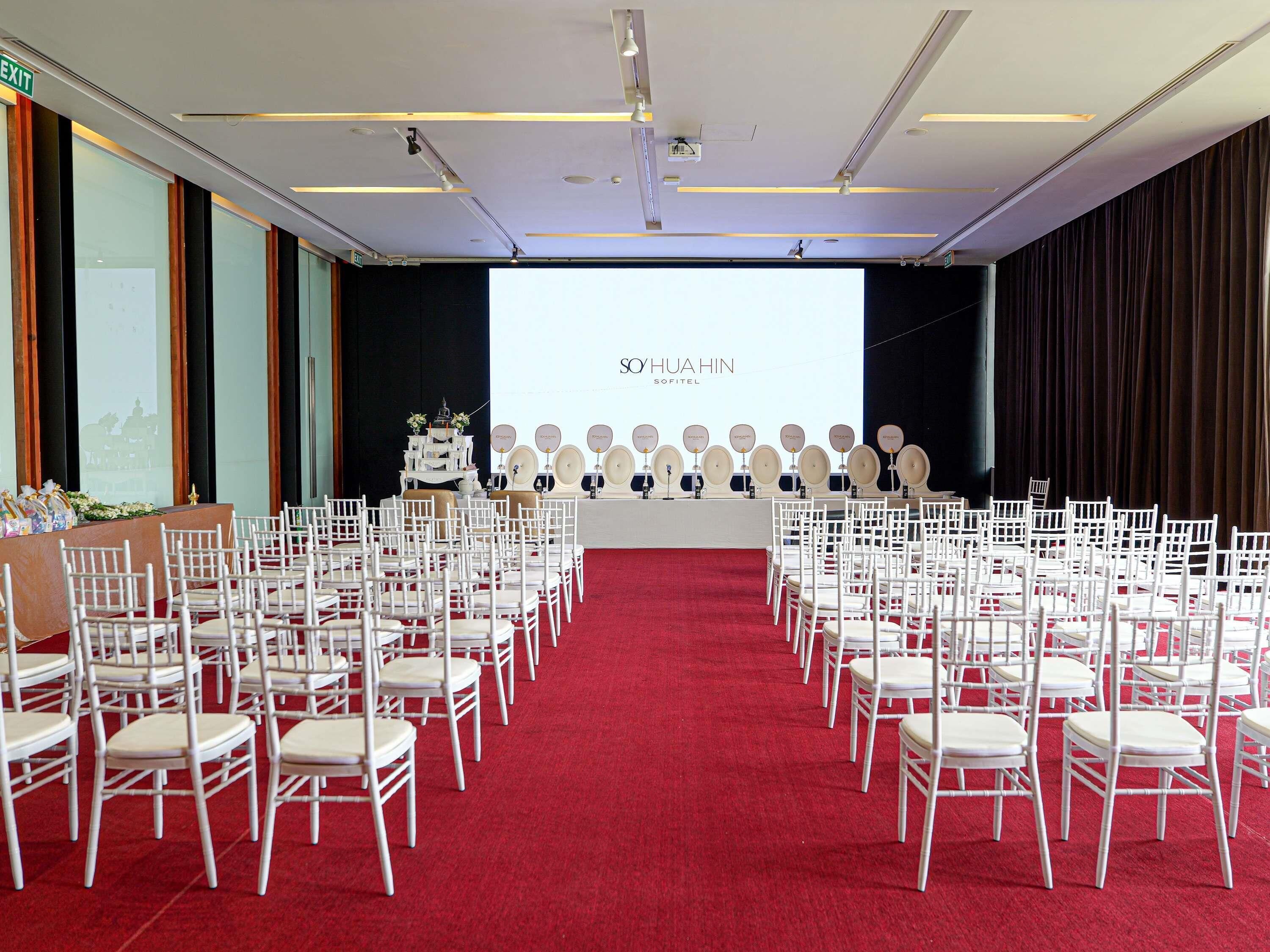 A conference room with rows of white chairs, a red carpet, and a projection screen displaying 'SOHUAHIN SOFITEL'.