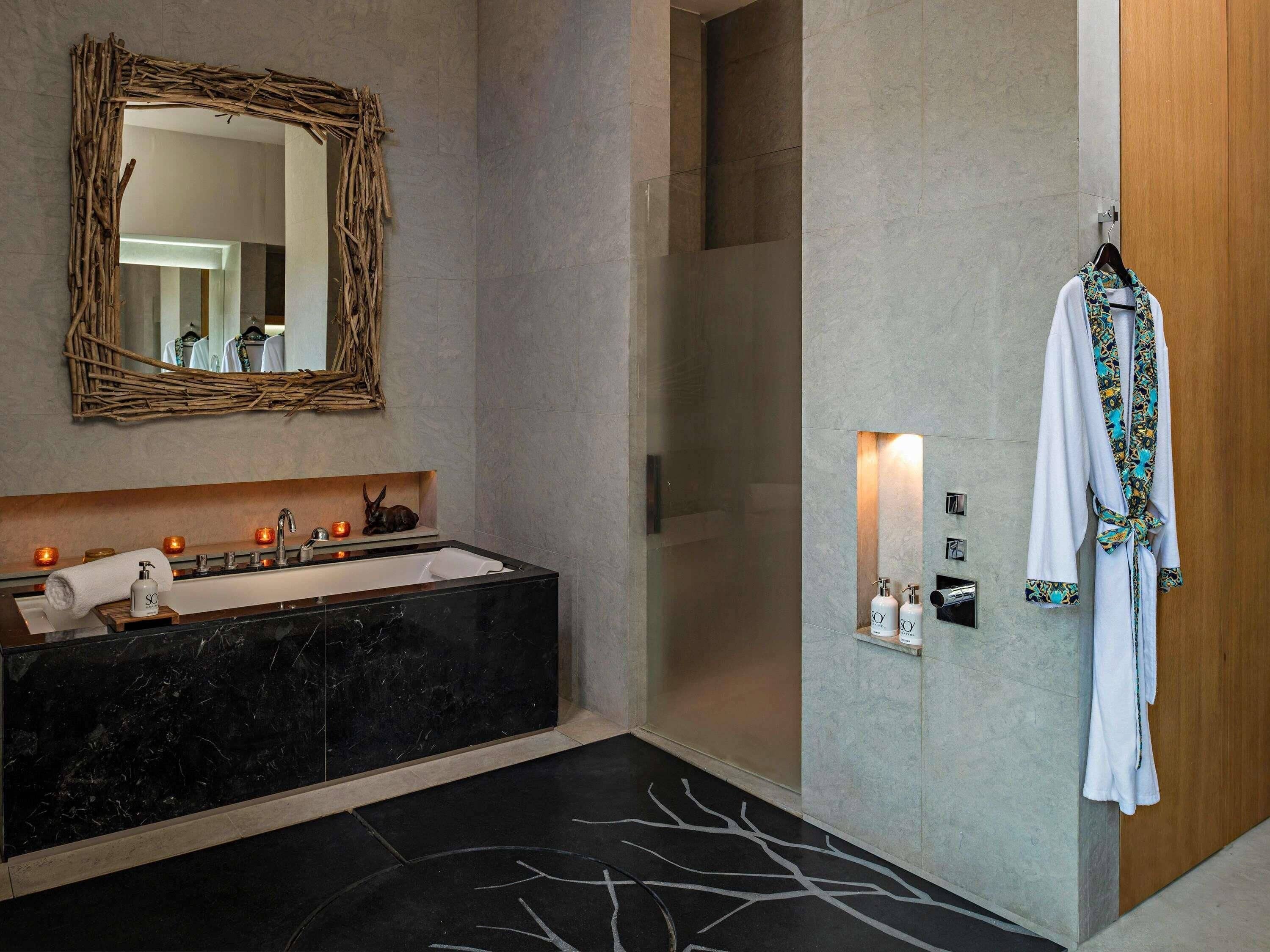 Un bagno con lavabo in marmo nero, uno specchio con cornice intrecciata, un accappatoio appeso a una porta in legno e un porta asciugamani a parete.