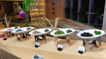 A buffet table with various dishes, a decorative plant, and a sign indicating the food options.