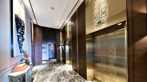 Un hall d’hôtel moderne avec un sol en marbre, un comptoir d’accueil et une œuvre d’art accrochée au mur.
