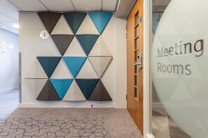 Una pared con un diseño geométrico, una puerta con el rótulo 'Meeting Rooms' y una alfombra con un patrón hexagonal.