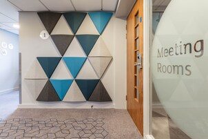 Una pared con un diseño geométrico, una puerta con el rótulo 'Meeting Rooms' y una alfombra con un patrón hexagonal.