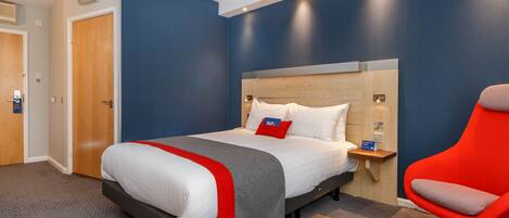 A hotel room with a bed, a nightstand, a red chair, and a wooden headboard.