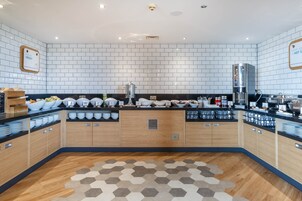 Cocina moderna con paredes de azulejos blancos, armarios de madera y una isla central con diversos alimentos y una máquina de café.