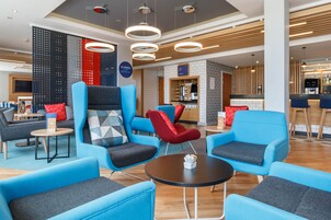 Un área de lounge moderna con asientos azules y grises, una máquina de café y una barra de desayuno.