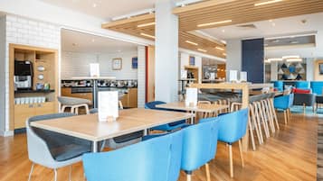 Un caffè moderno con tavoli di legno e sedie blu, una macchina da caffè e una bacheca con il menu.