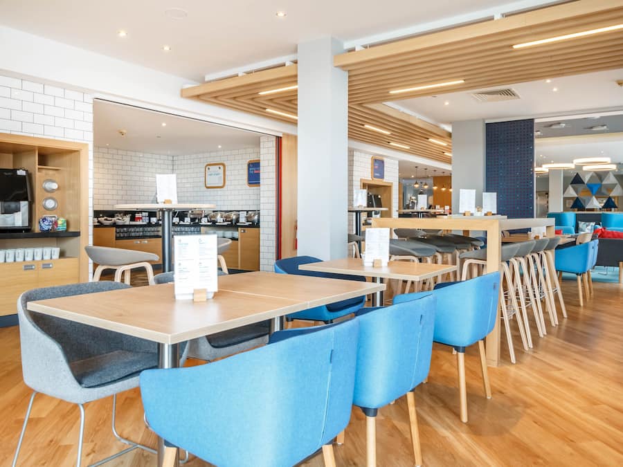 Un café moderno con mesas de madera y sillas azules, una máquina de café y una pizarra con el menú.