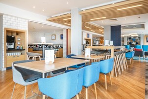 Un café moderno con mesas de madera y sillas azules, una máquina de café y una pizarra con el menú.