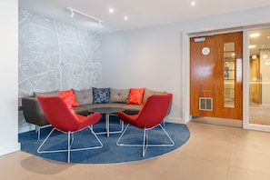 A modern office space with a curved sofa, two red chairs, and a round table.