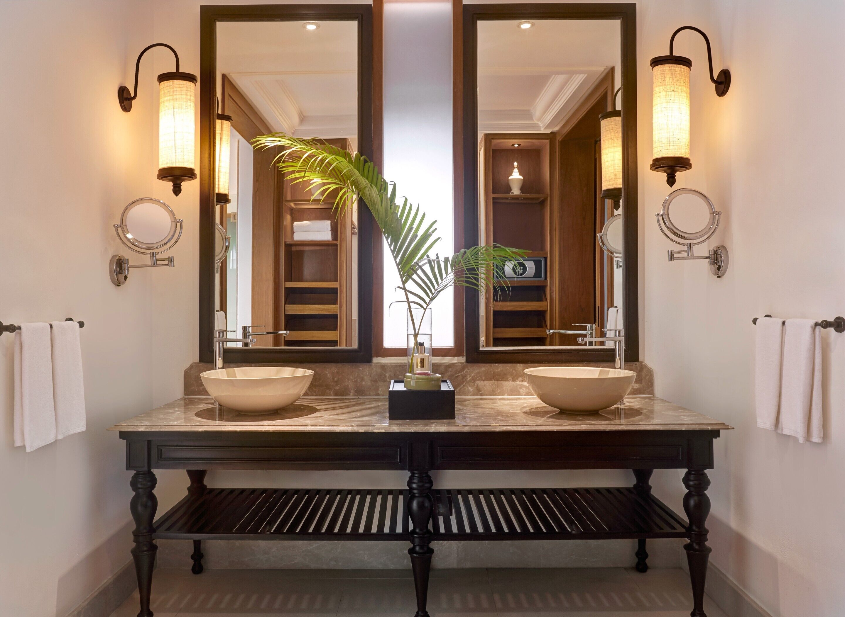 A bathroom with a large vanity, two sinks, a mirror, wall sconces, and a plant.