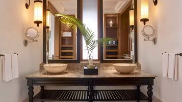 A bathroom with a large vanity, two sinks, a mirror, wall sconces, and a plant.