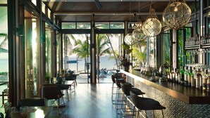 A modern bar area with a view of the ocean, large windows, and hanging spherical light fixtures. - Santiburi Koh Samui (Koh Samui)