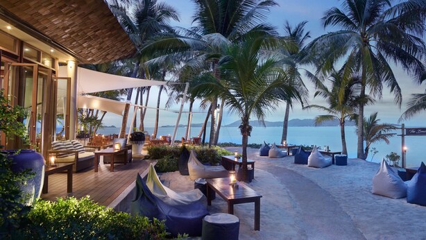 A beachside lounge with seating and tables, palm trees, and a view of the ocean. - Santiburi Koh Samui (Koh Samui)