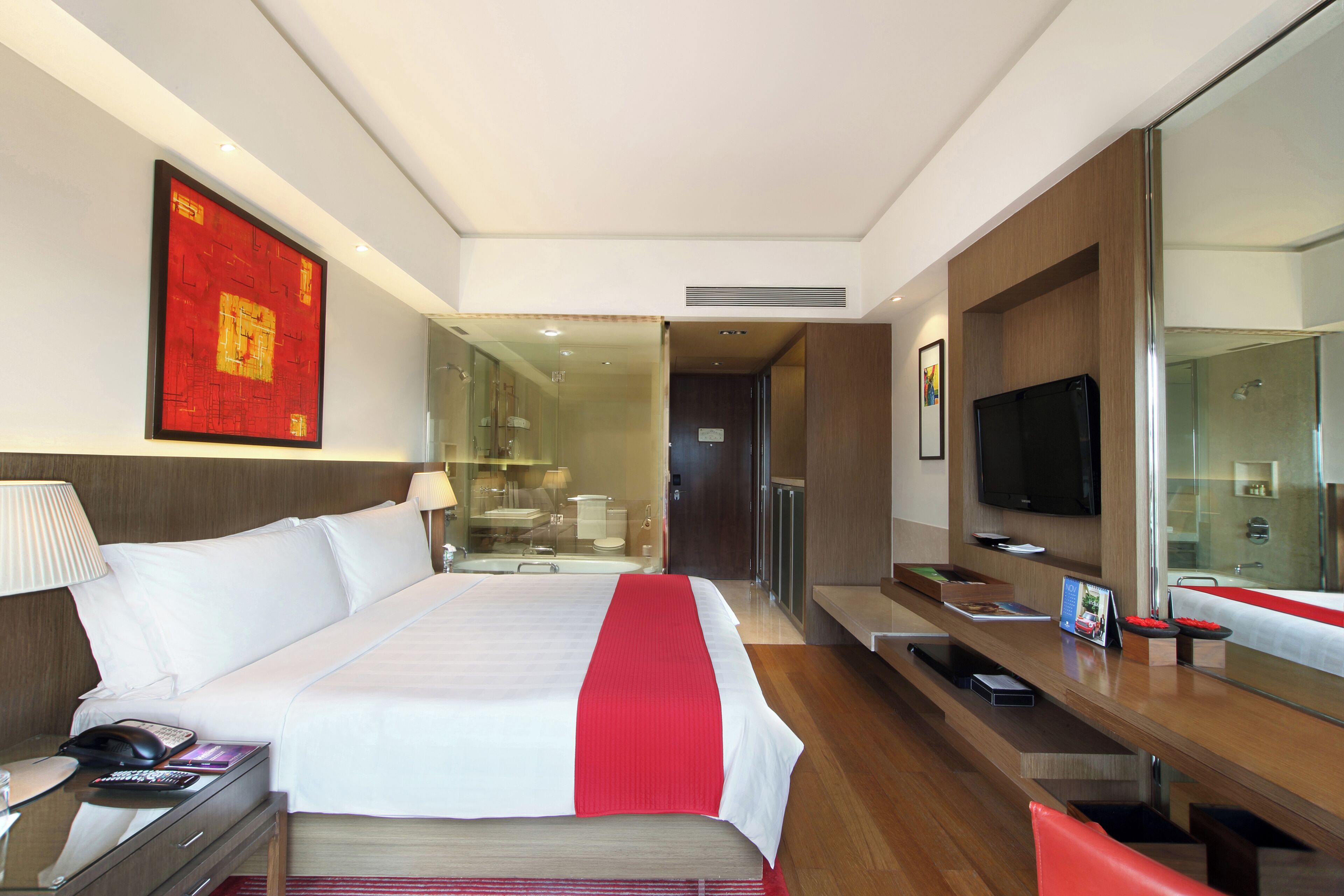 A hotel room with a bed, bedside table, TV, and a large mirror.