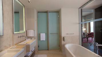 Un baño moderno con una bañera grande, dos lavamanos, un espejo y una puerta que da a la zona de la ducha.