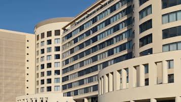 Un hôtel à plusieurs étages, doté d’une façade incurvée, de grandes fenêtres et d’un parking où se trouve une voiture noire.