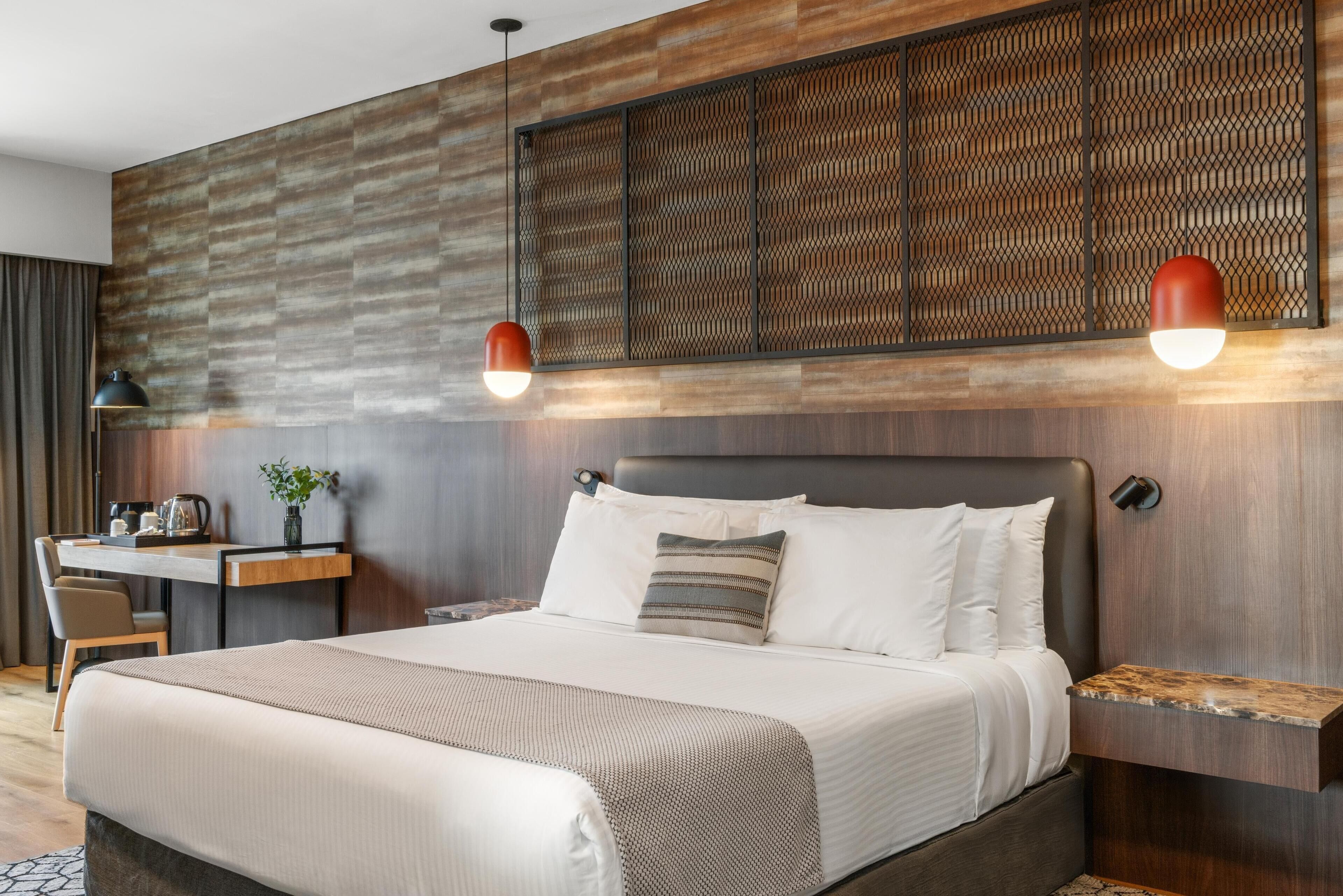 A modern hotel room with a large bed, a desk, and a wall-mounted light fixture.
