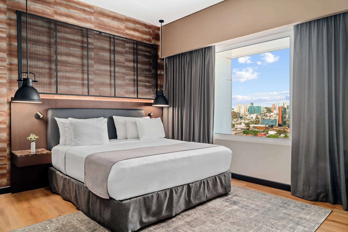 Una habitación de hotel moderna con una cama grande, vistas a la ciudad y un panel decorativo de madera.