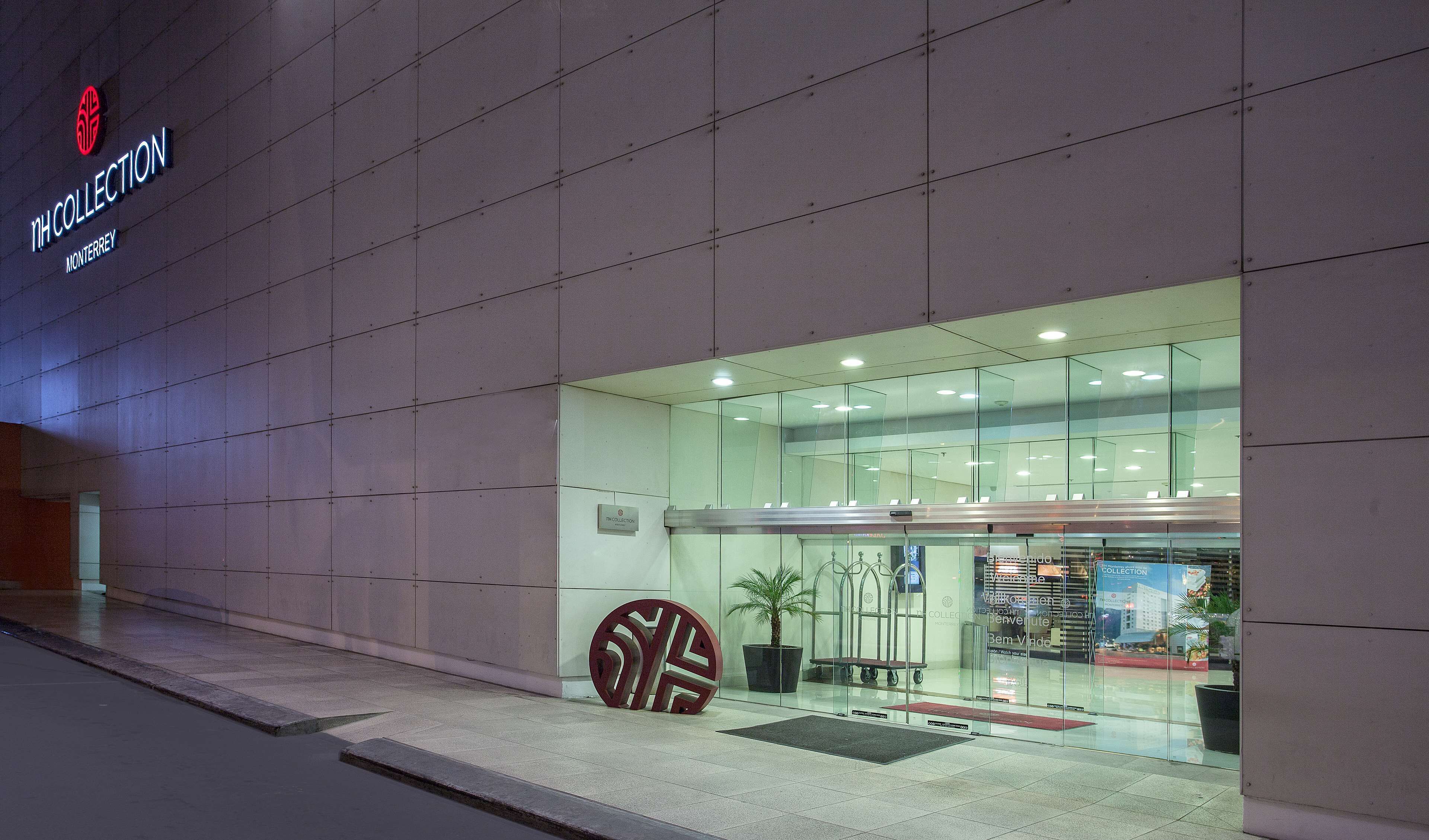 A modern building with a glass entrance, a large decorative metal piece, and a sign reading "IH COLLECTION MONTERREY".