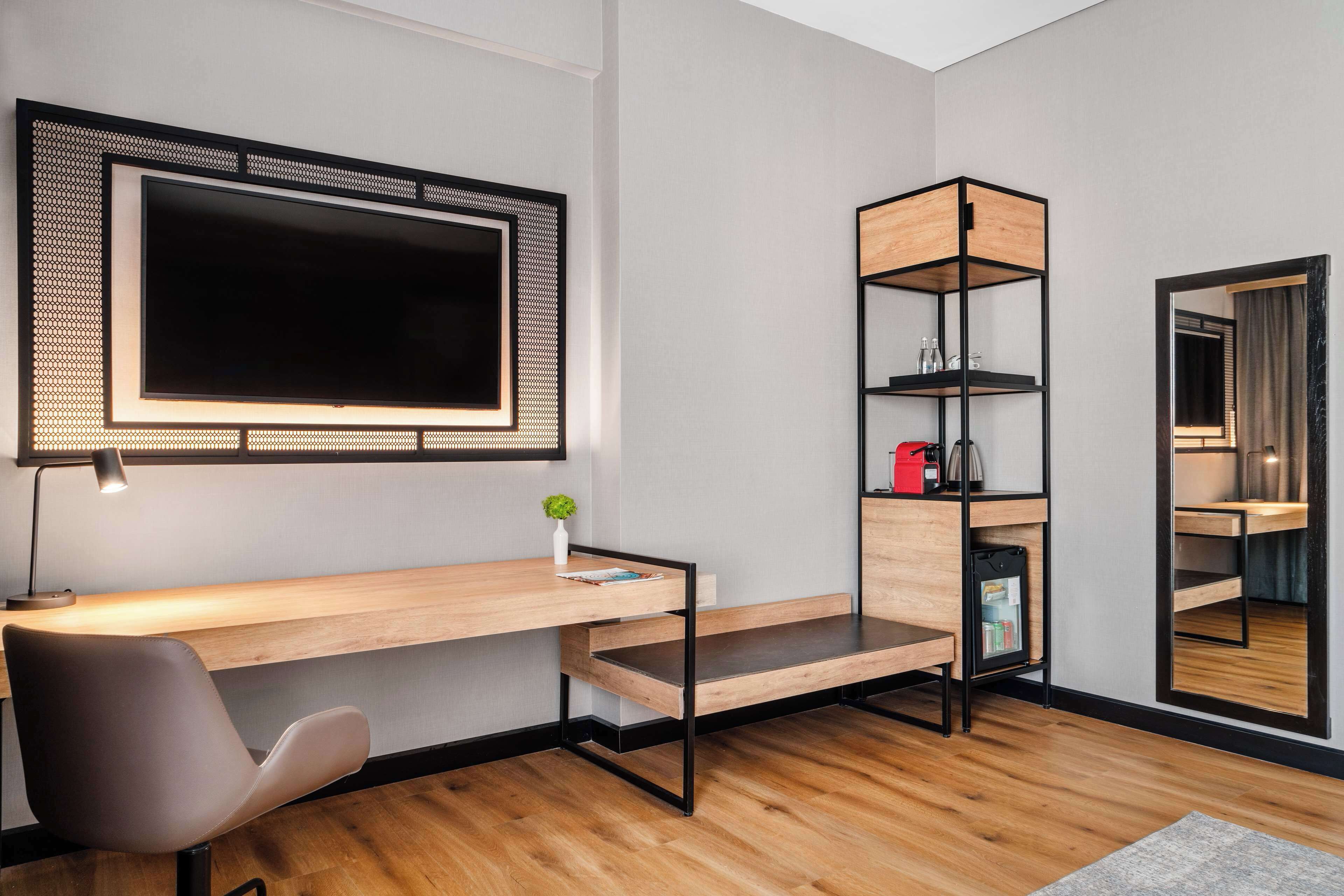 A modern room with a wooden desk, a chair, a TV mounted on the wall, and a tall shelving unit.