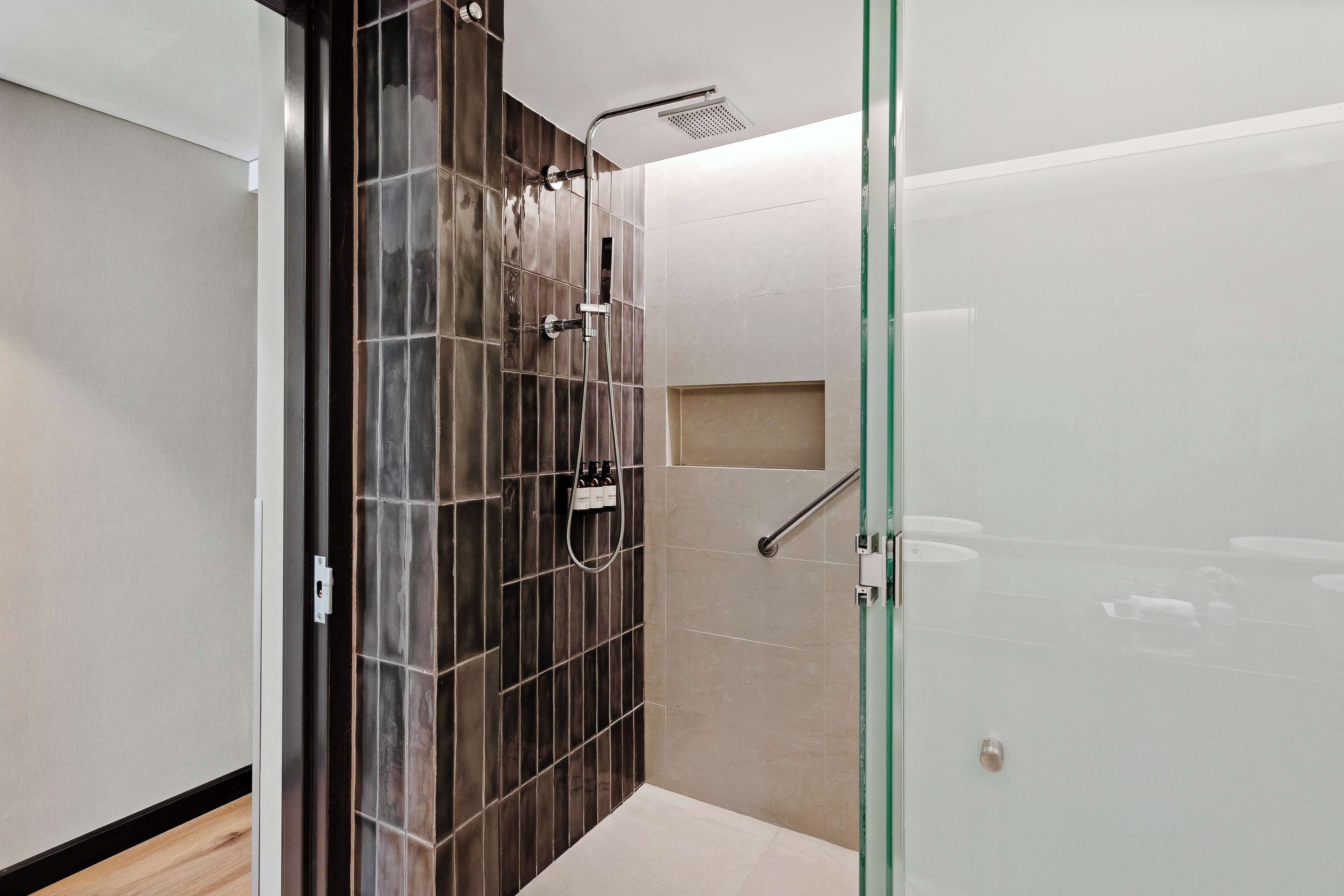 A modern bathroom with a glass shower enclosure, a wooden accent wall, and a beige tiled floor.