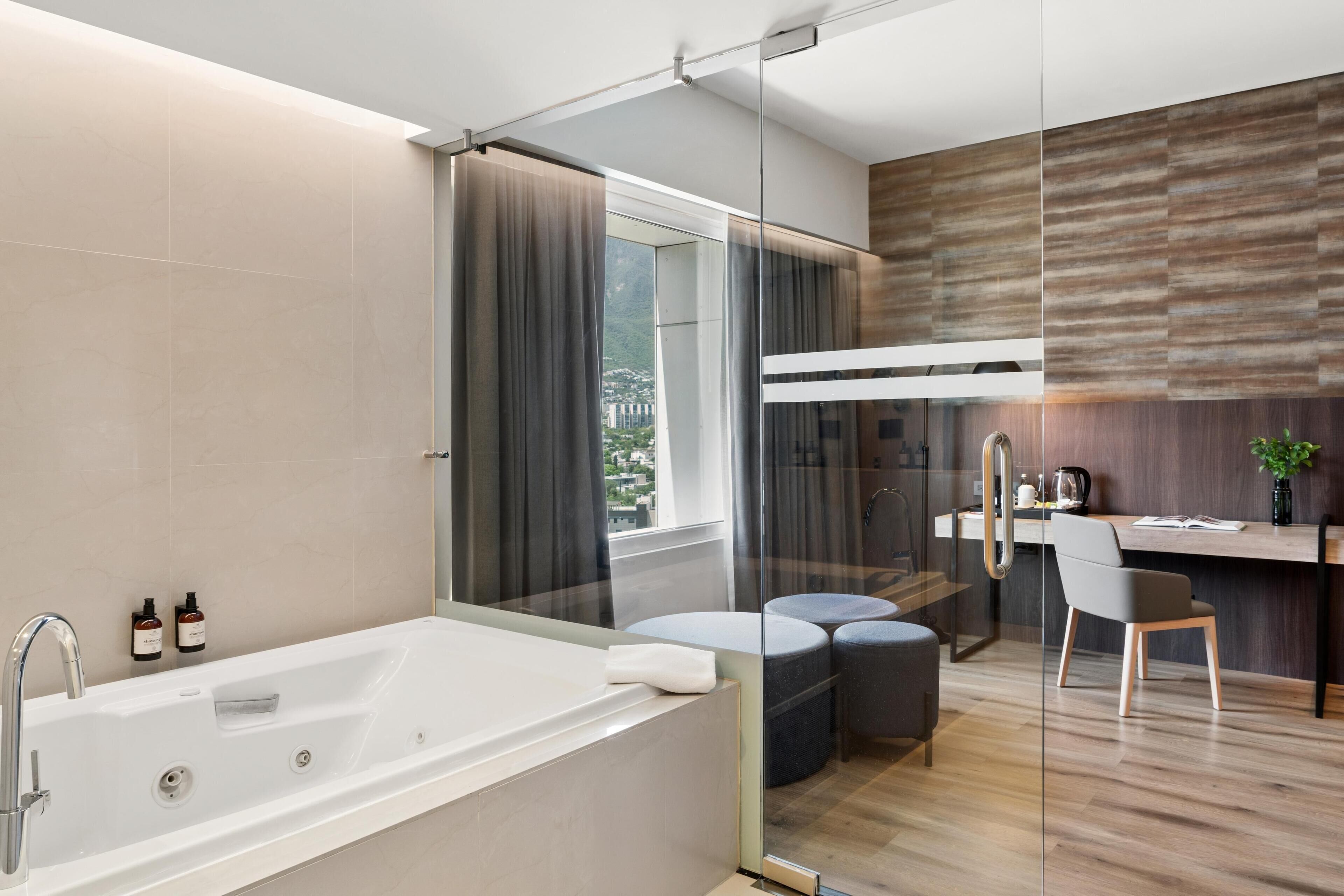 A modern bathroom with a bathtub, a shower, and a glass-enclosed desk area with a chair and a small table.