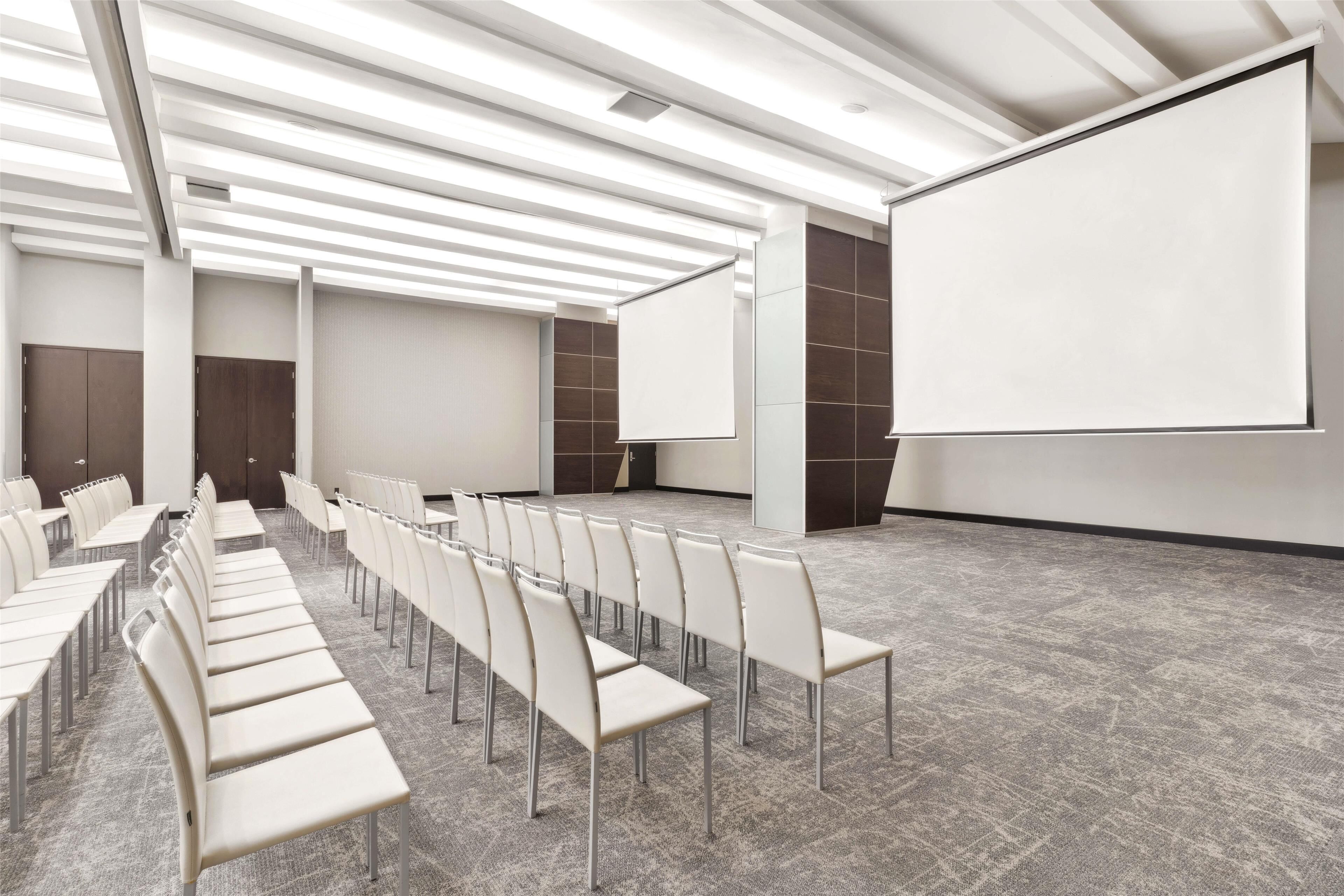 A conference room with rows of chairs, a large projection screen, and a carpeted floor.