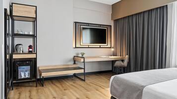 A hotel room with a bed, a desk, a chair, a television, and a minibar.