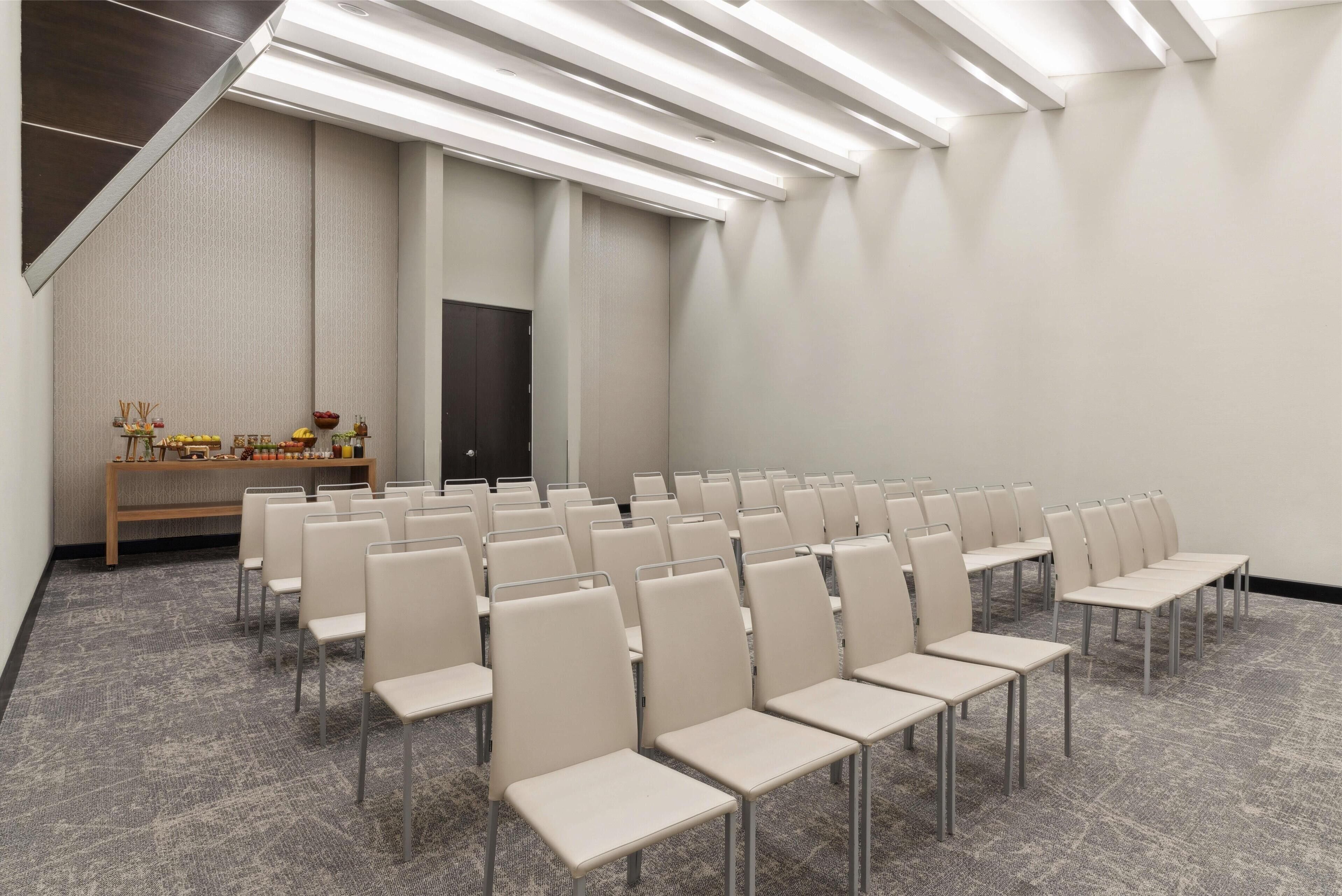 A conference room with rows of chairs, a wooden bench with items, and a door.