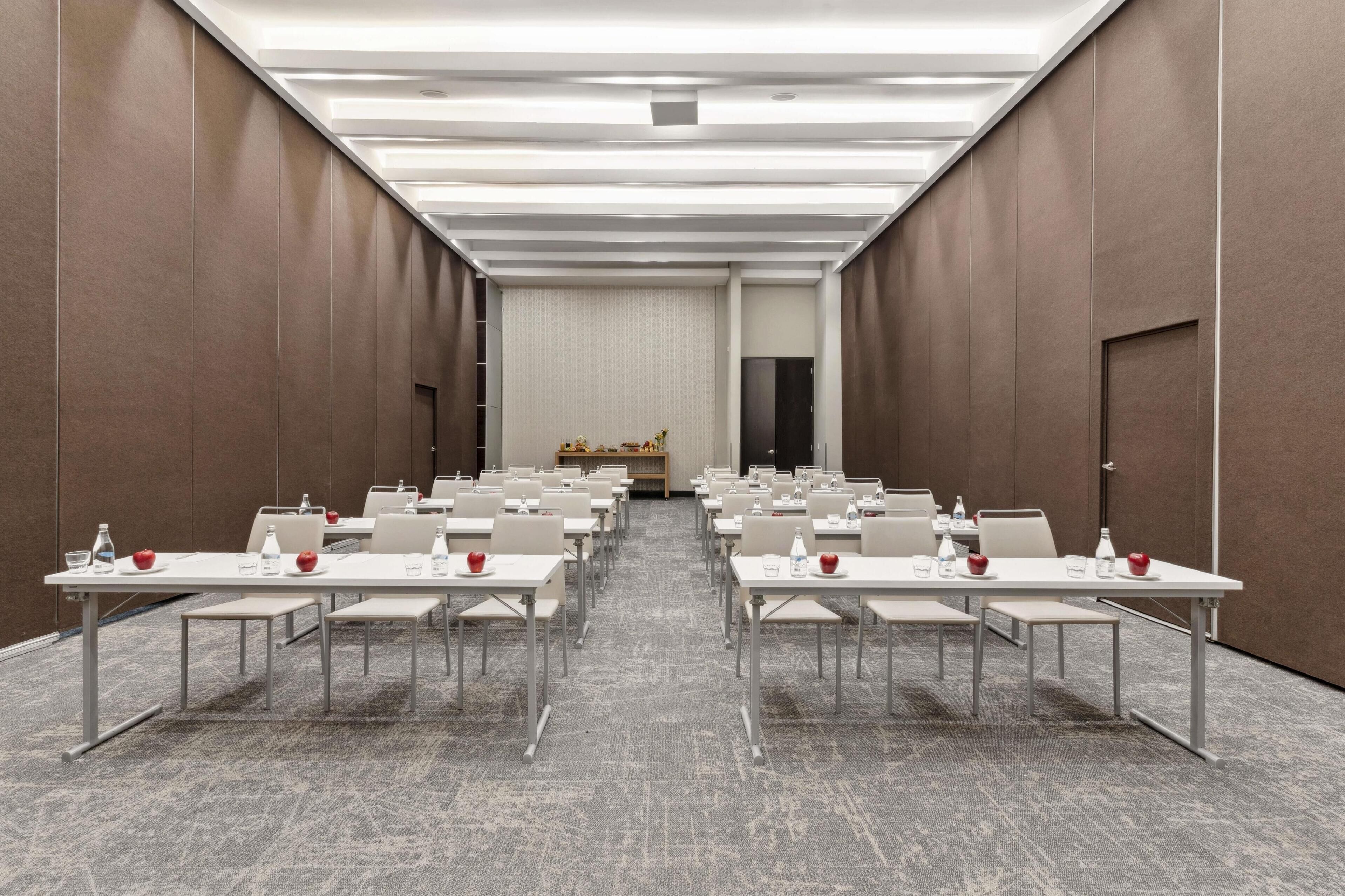 A conference room with rows of tables and chairs, a podium, and a carpeted floor.