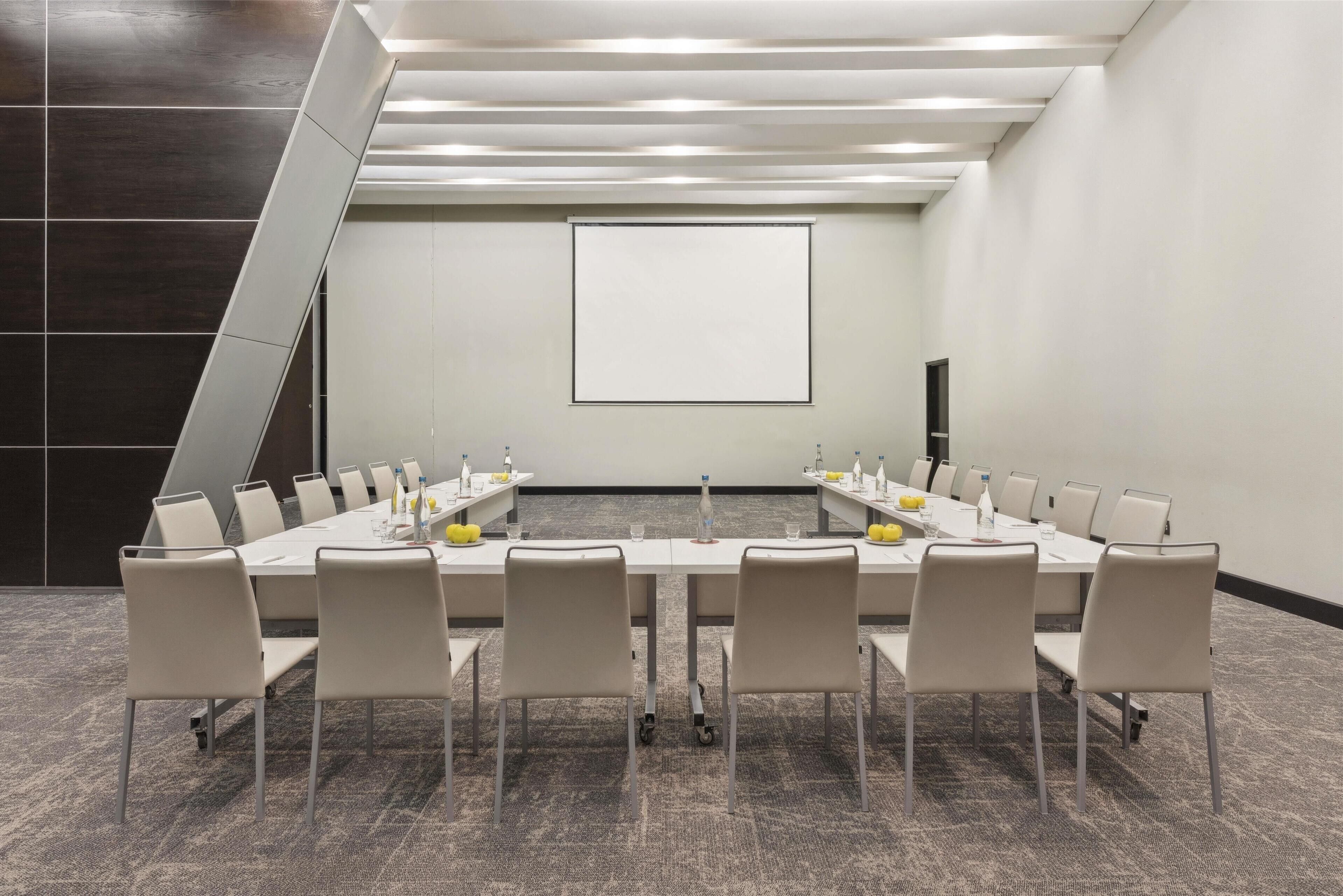 A conference room with a long table, chairs, and a projector screen.
