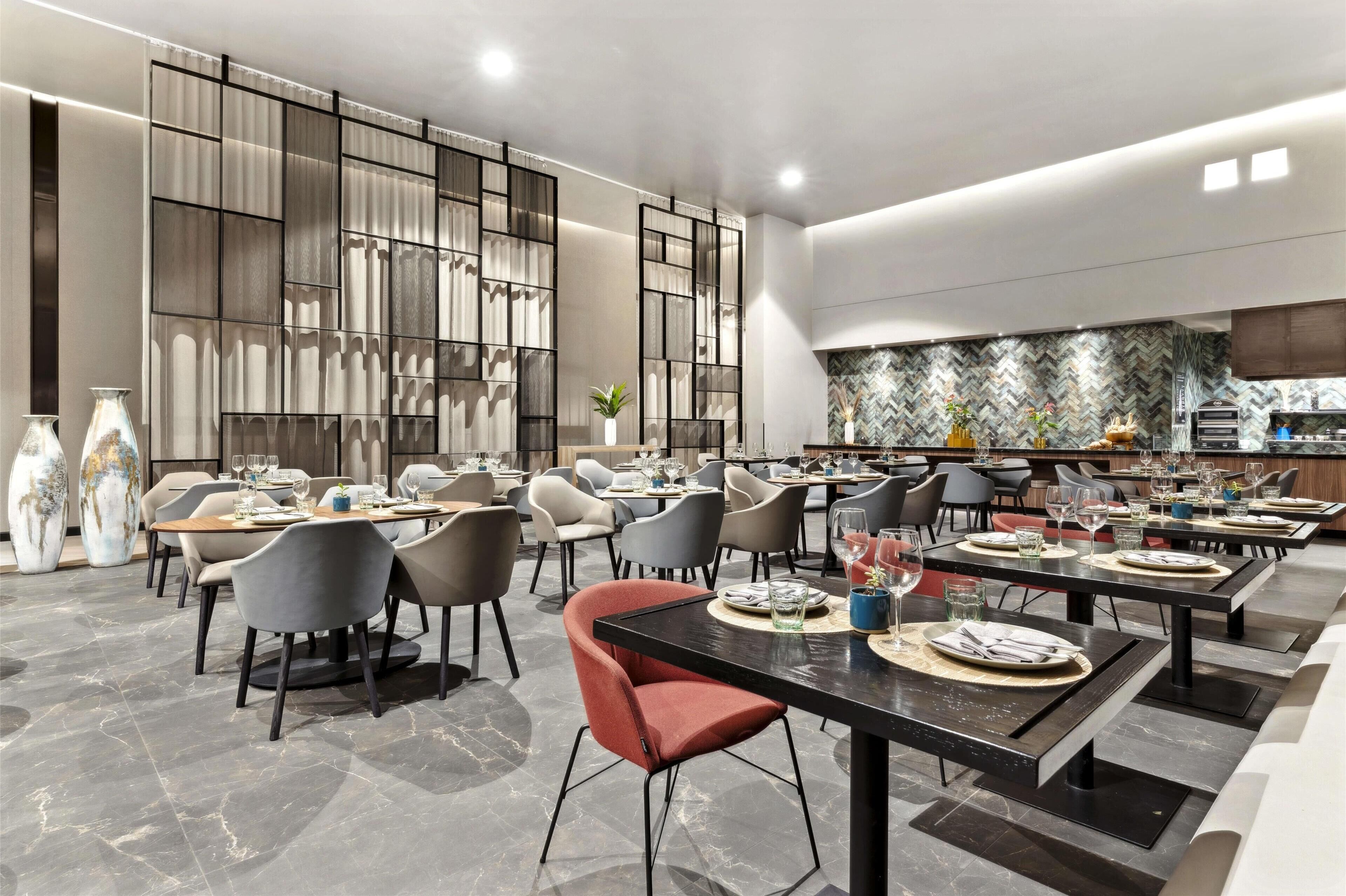 A modern restaurant with multiple dining tables and chairs, a kitchen area, and decorative vases.