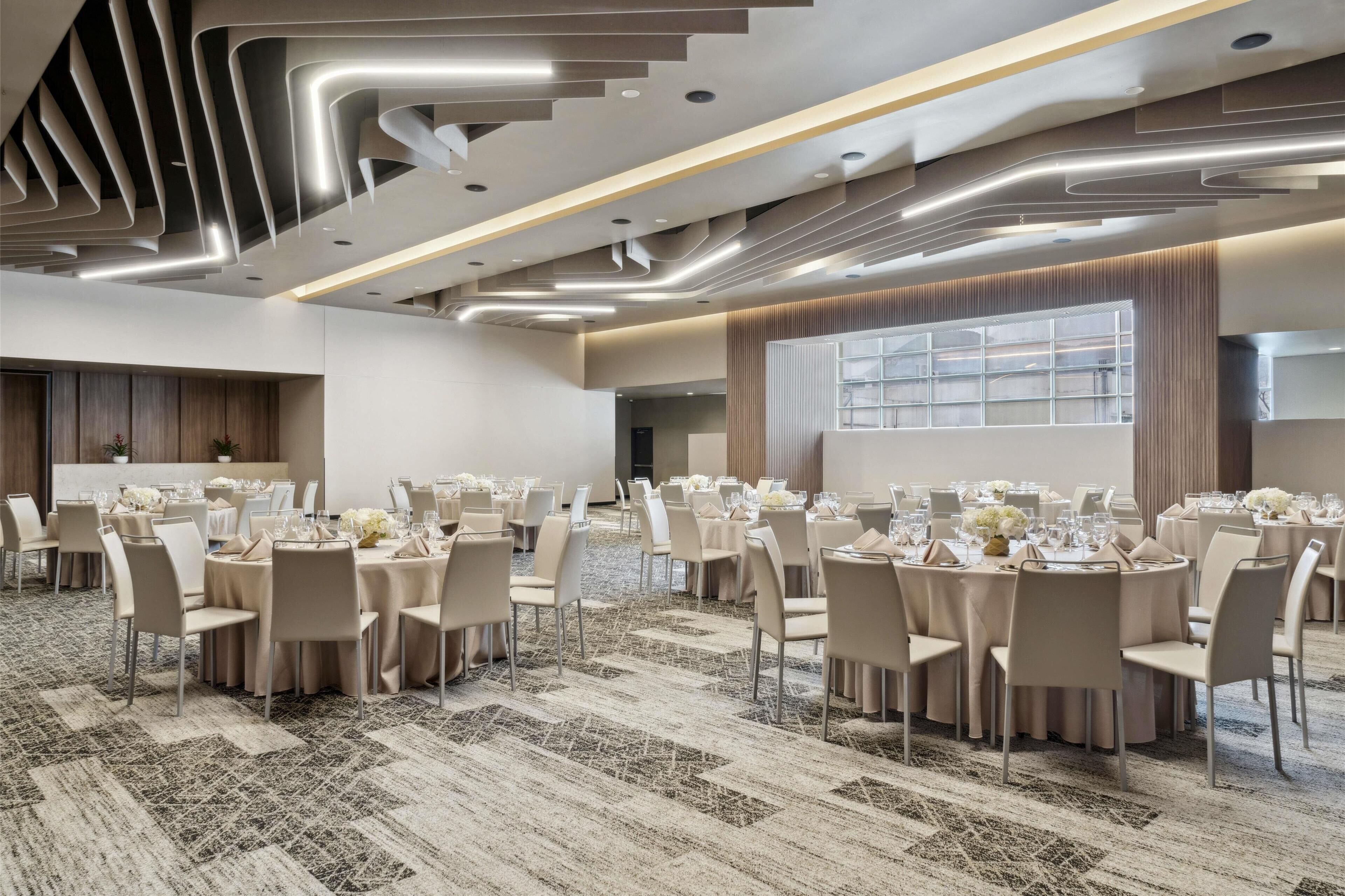 Une salle de conférence moderne, dotée de tables rondes, de chaises de couleur beige et d’un tapis à motifs.