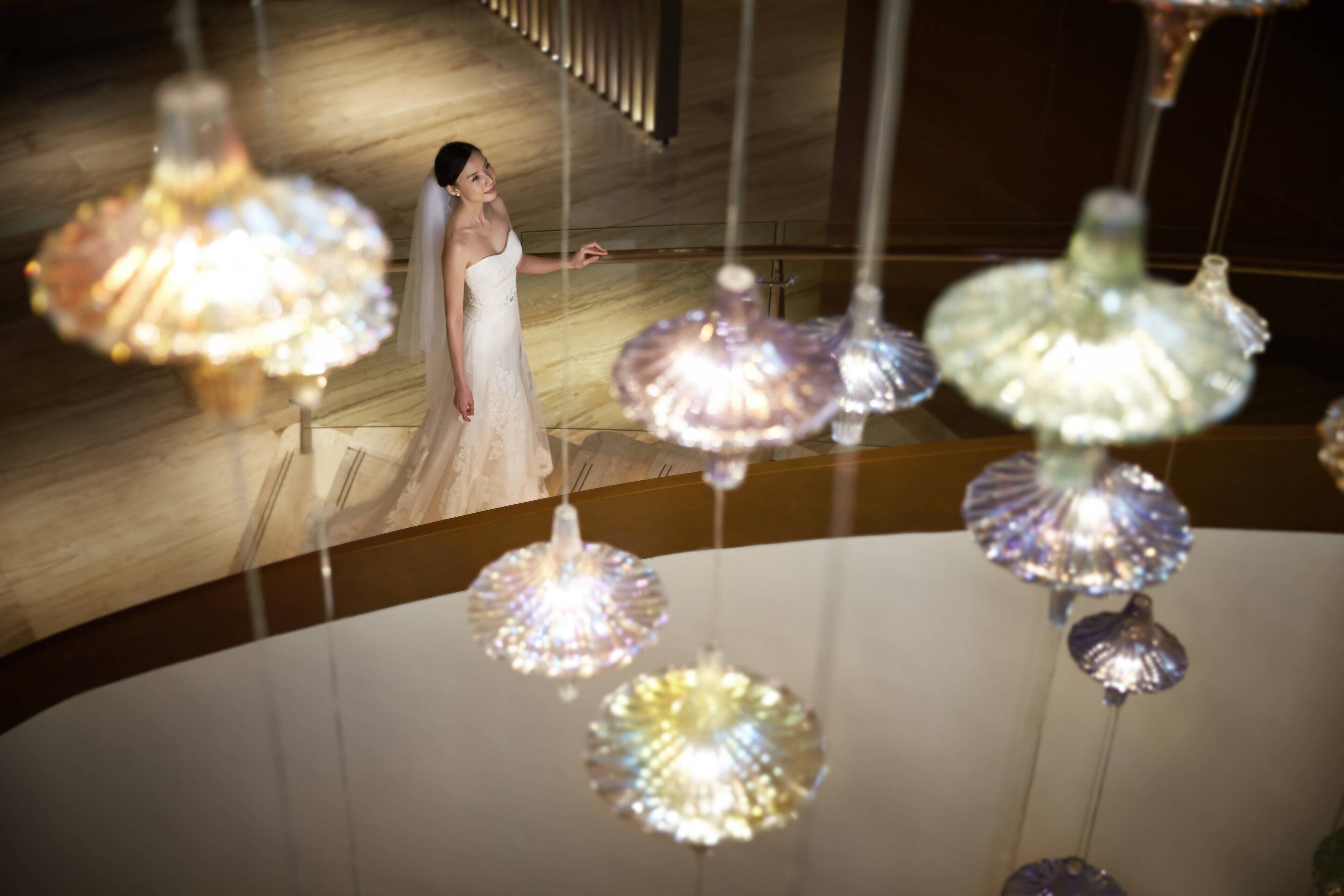A person in a white dress standing in a room with hanging glass light fixtures.