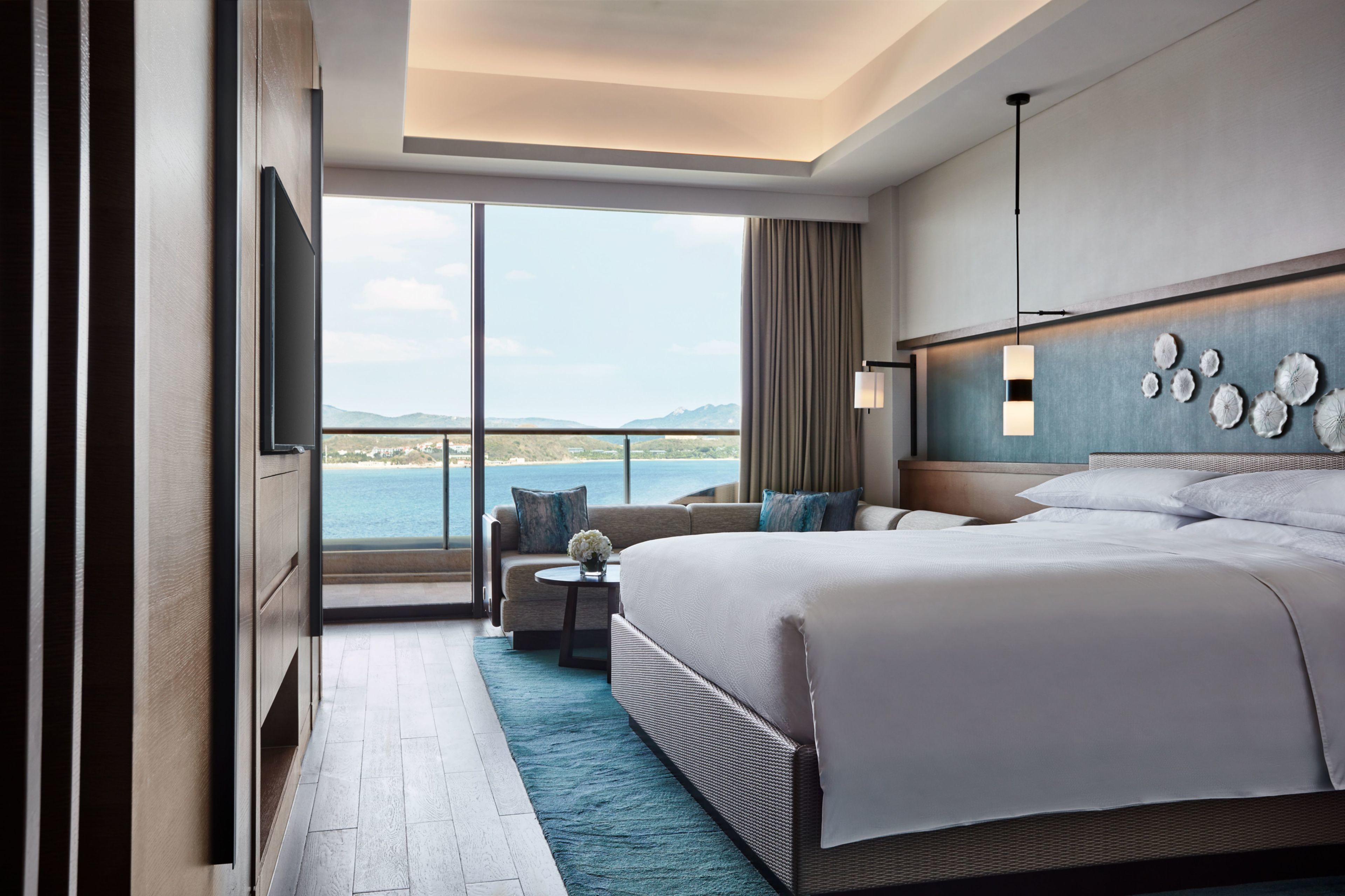 Una habitación de hotel moderna con una cama grande, un sofá, una mesita con un jarrón y vistas al mar.