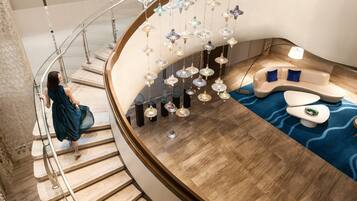 A modern interior with a curved staircase, a seating area with a blue patterned rug, and hanging decorative lights.