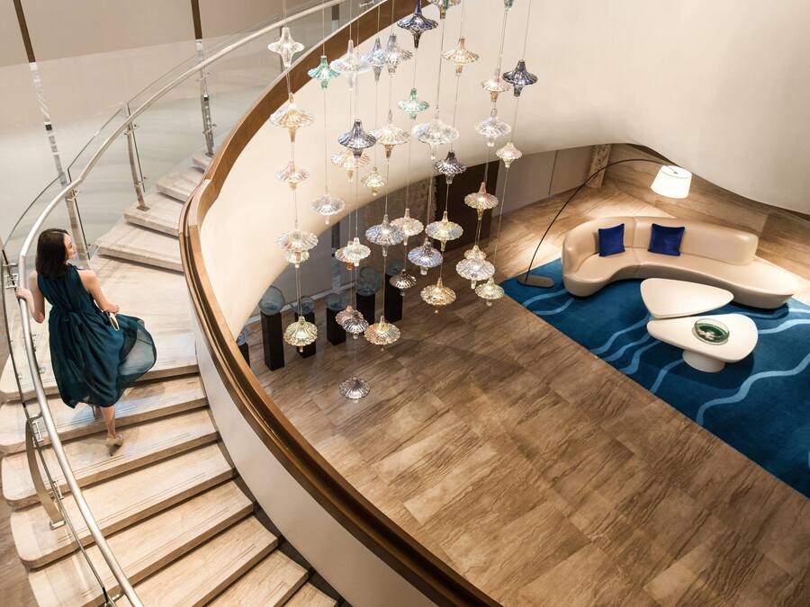 A modern interior with a curved staircase, a seating area with a blue patterned rug, and hanging decorative lights.