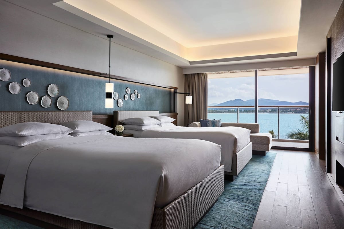 A modern hotel room with two beds, a large window with a city and mountain view, and a decorative wall with circular patterns.