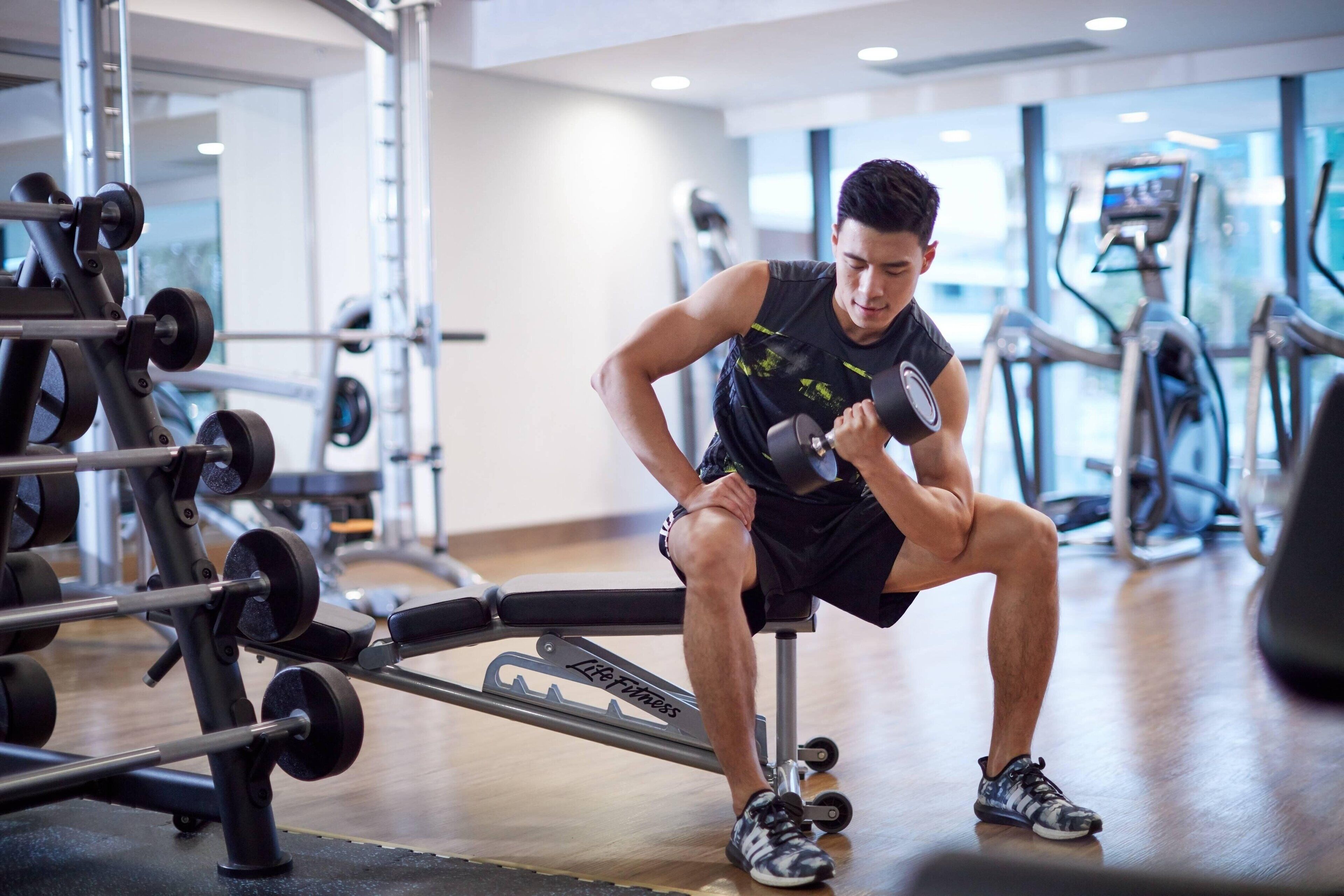 Un gimnasio con equipo de levantamiento de pesas, cintas de correr y una banca.