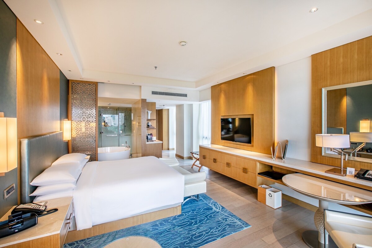 Una habitación de hotel moderna con una cama grande, un baño con espejo y un escritorio con silla.