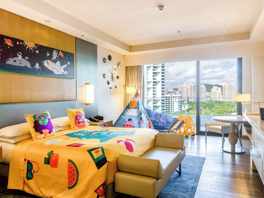 Habitación de hotel con una cama grande, un escritorio, una silla, un ventanal con vistas a la ciudad y un cuadro en la pared.
